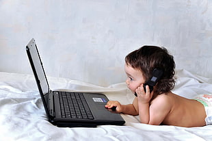 toddler with phone using laptop